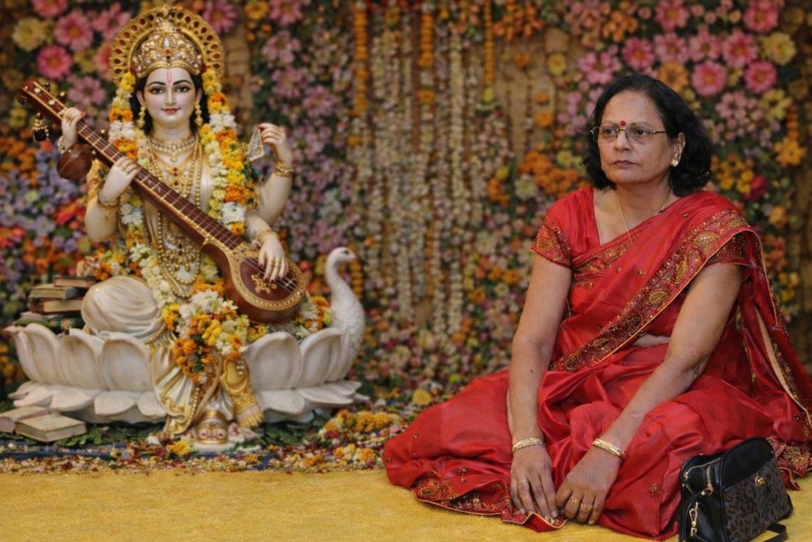 Seated beside a Goddess Saraswati display at a festive event